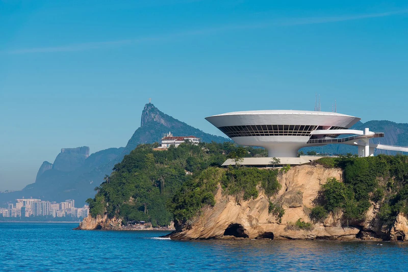 The saucer-shaped MAC Niterói on its clifftop over Guanabara Bay, with Christ the Redeemer in the distance